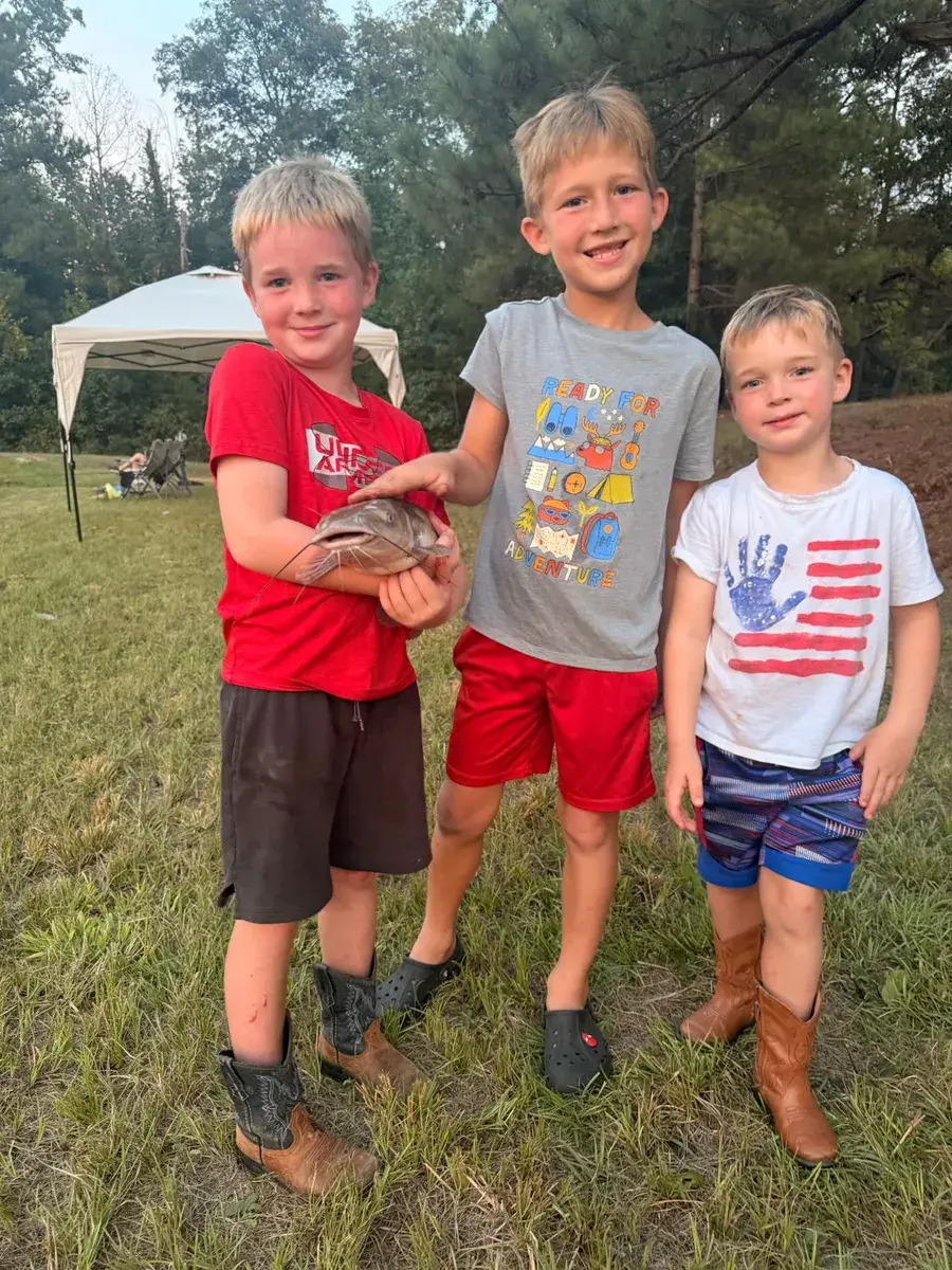 Three boys in a field, one holding a catfish they caught
